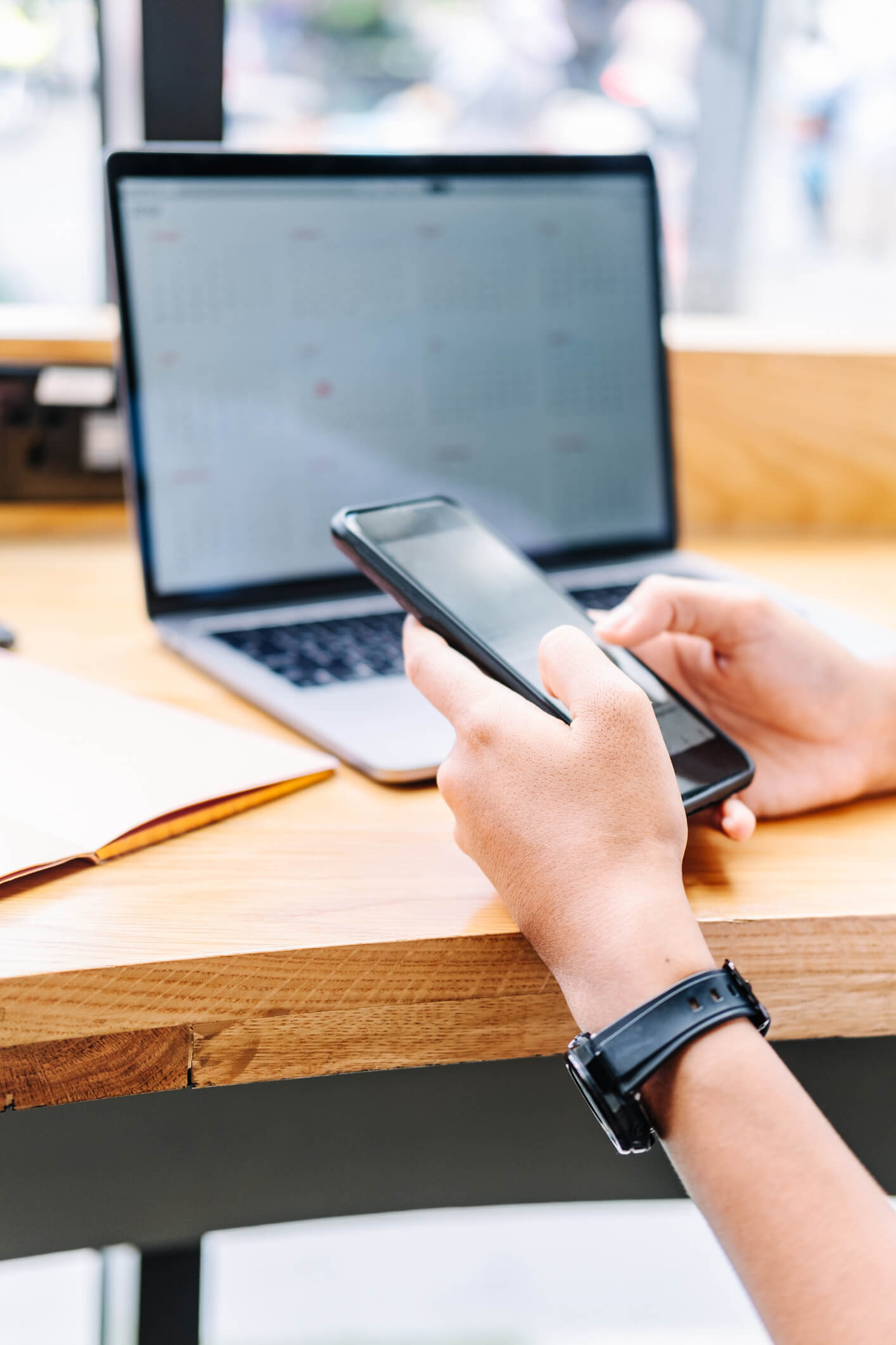 person holding phone with a laptop on their desk